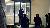 Still image of Protesters breaking bank doors down.